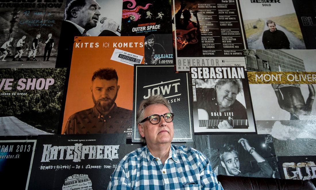 Daglig leder Anton Bjerg sidder i backstagerummet på spillestedet Generator. Over ham hænger plakater fra et par af de kunstnere, der hat stået på scenen de seneste otte år. 